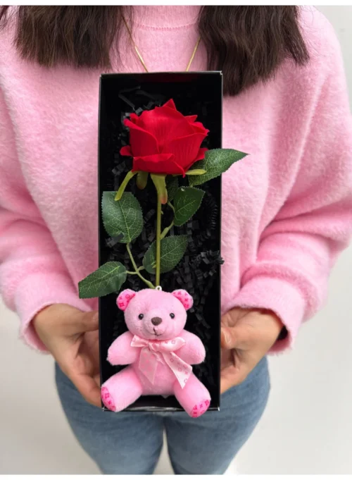 Pembe kazak tutan kişinin elinde kırmızı gül ve pembe ayıcık kutulu hediye
